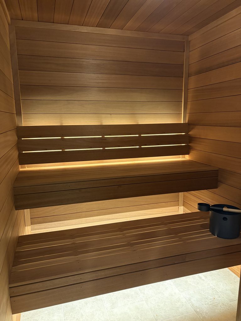 Ambara sauna interior with warm golden-brown paneling, backrest lighting and sauna bucket
