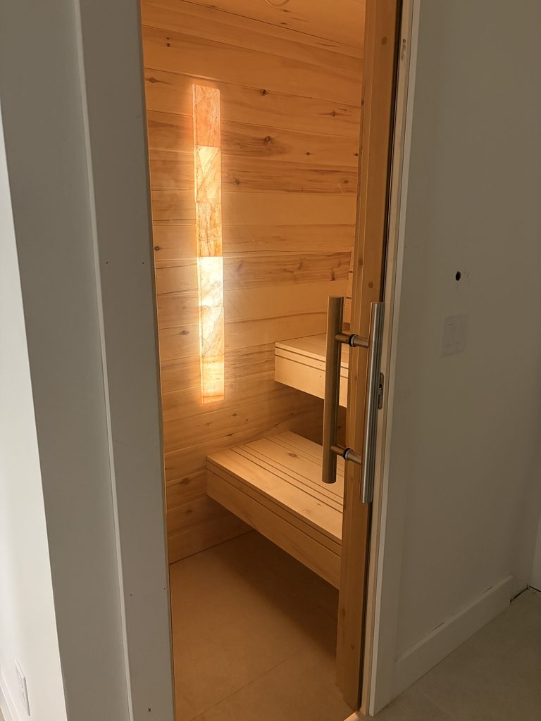 View into the Aspen sauna through the open glass door showing benches and salt brick accent lighting